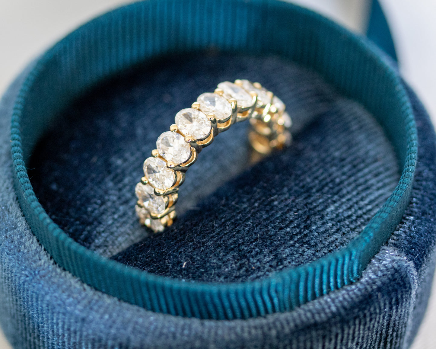 Oval-cut diamond eternity band nestled in teal ribbon, close angle