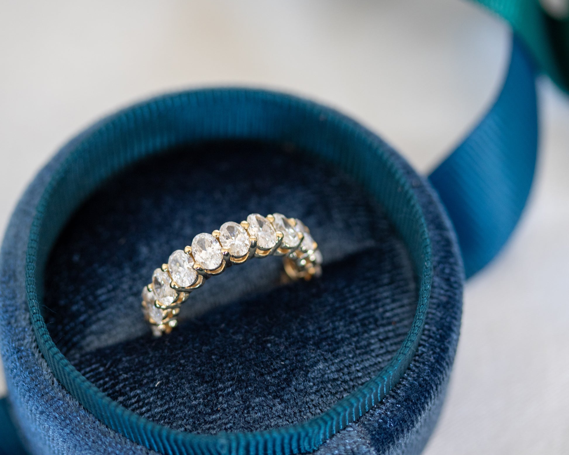 Oval-cut diamond eternity band resting on a coiled teal ribbon
