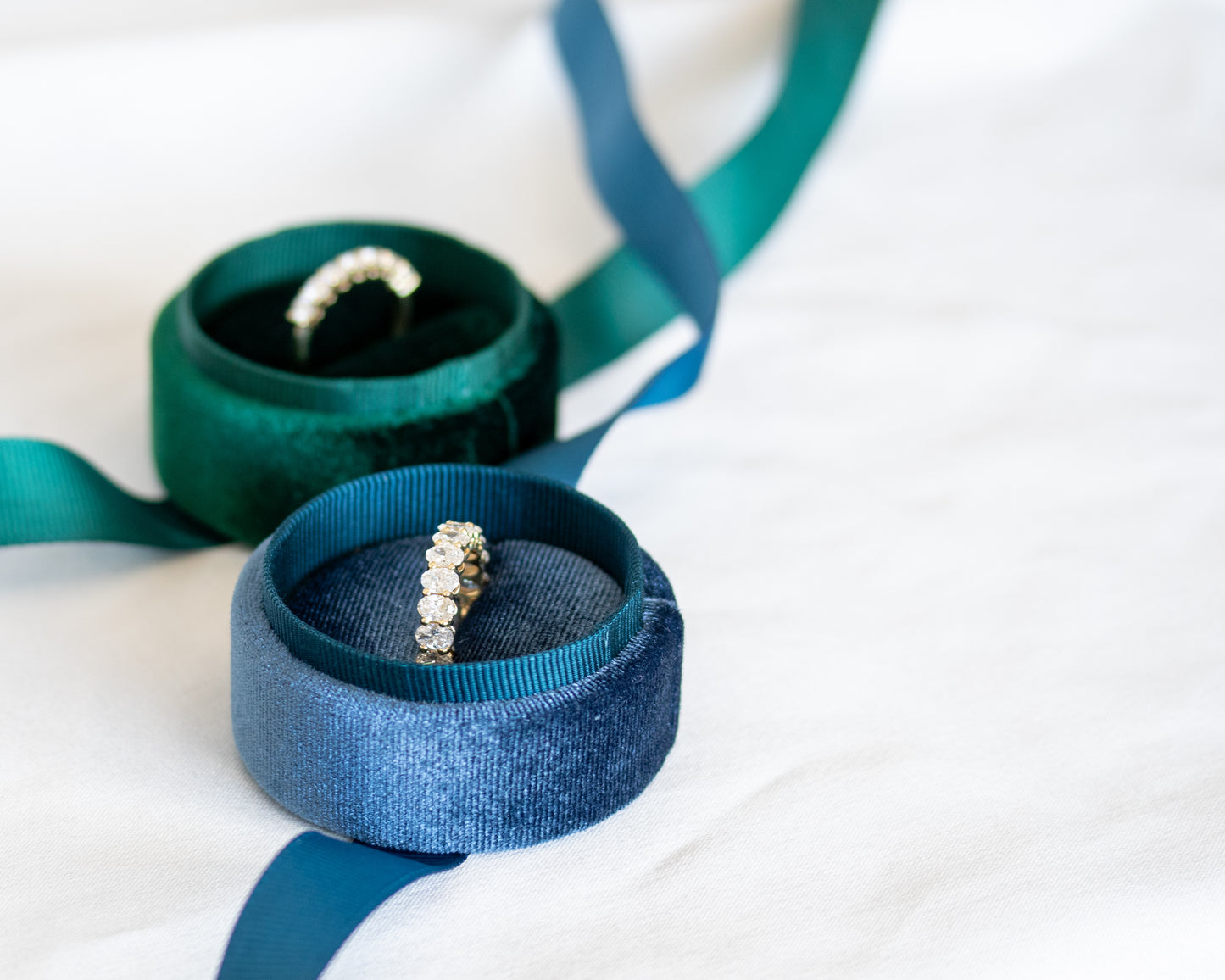 Oval-cut diamond eternity band on teal ribbon with soft white fabric backdrop