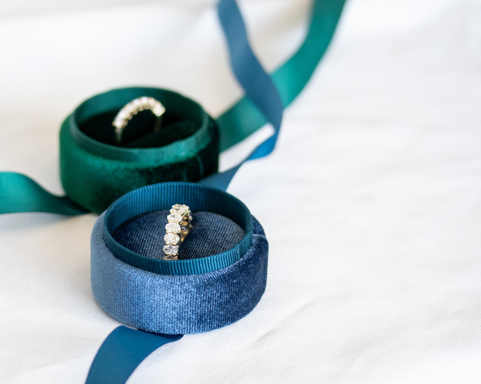 Oval-cut diamond eternity band on teal ribbon with soft white fabric backdrop
