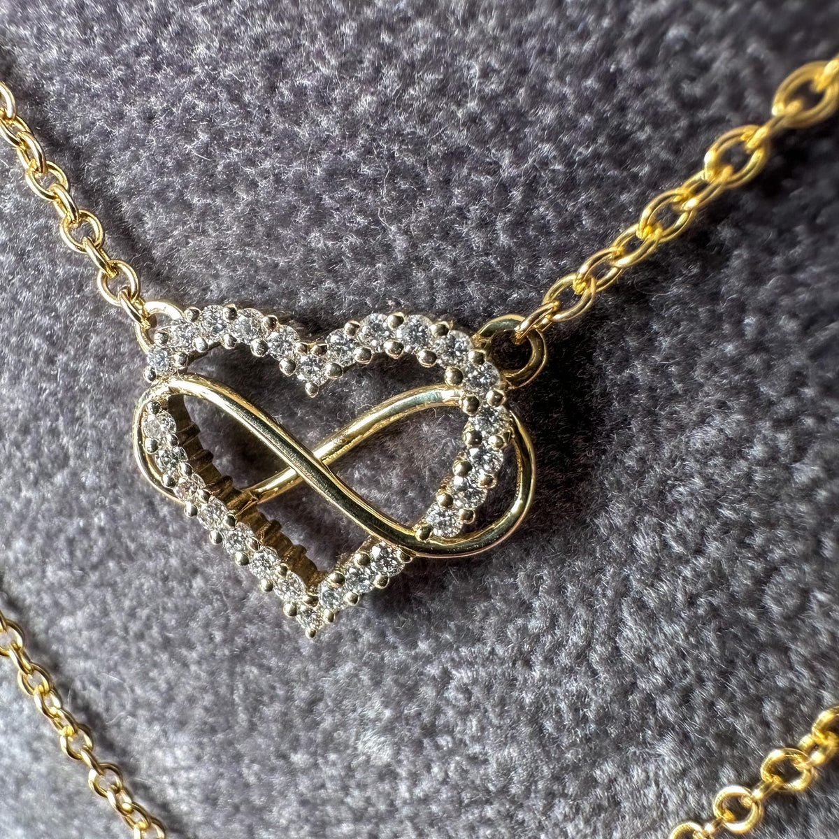 Close-up of a diamond-set heart wrapped in a gold infinity loop on a gray textured background
