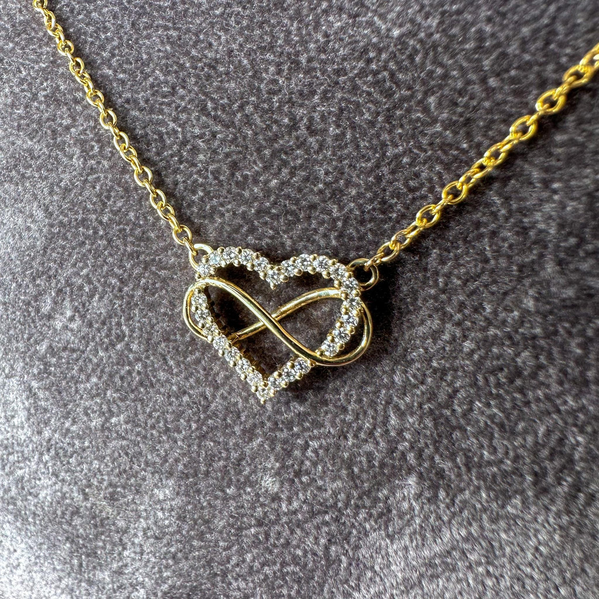 Open heart set with round diamonds and a gold infinity loop on a gray textured background