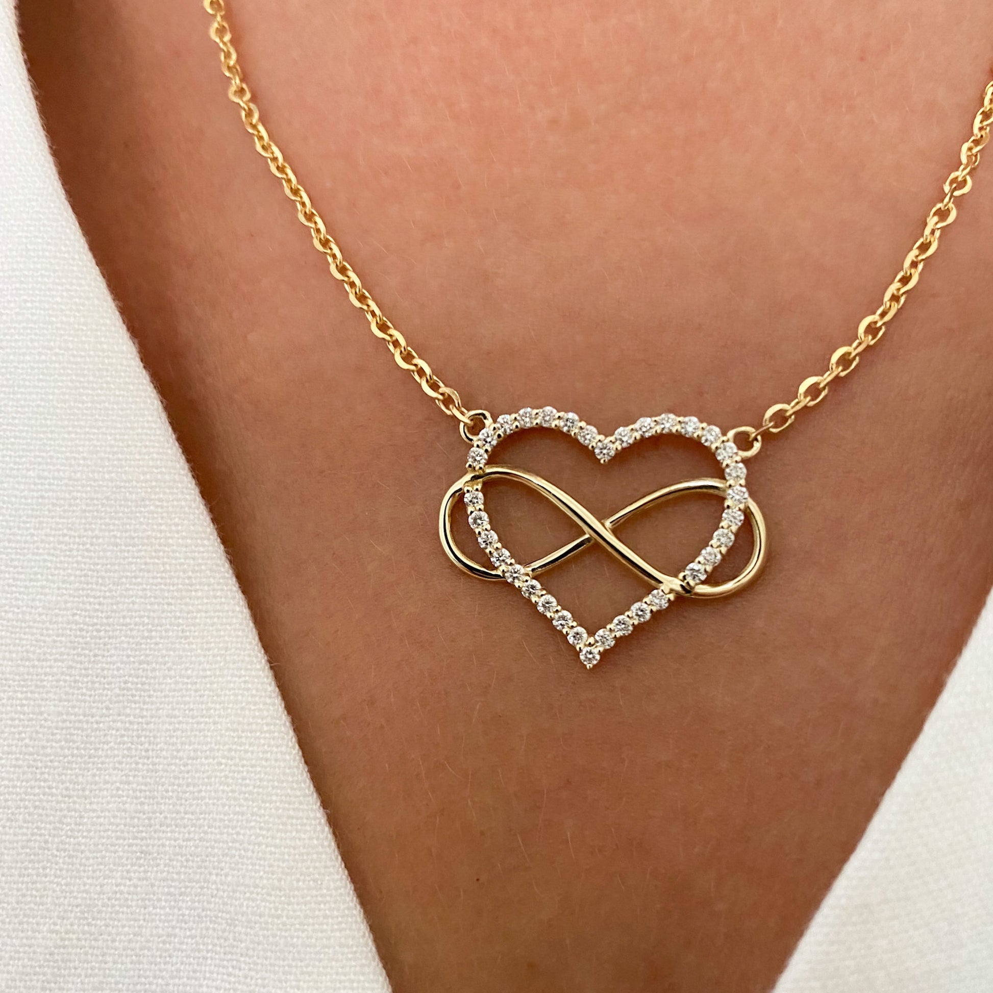 A heart-shaped pendant necklace with a diamonds and gold infinity symbol, attached to a yellow gold chain, displayed on a person's neck.
