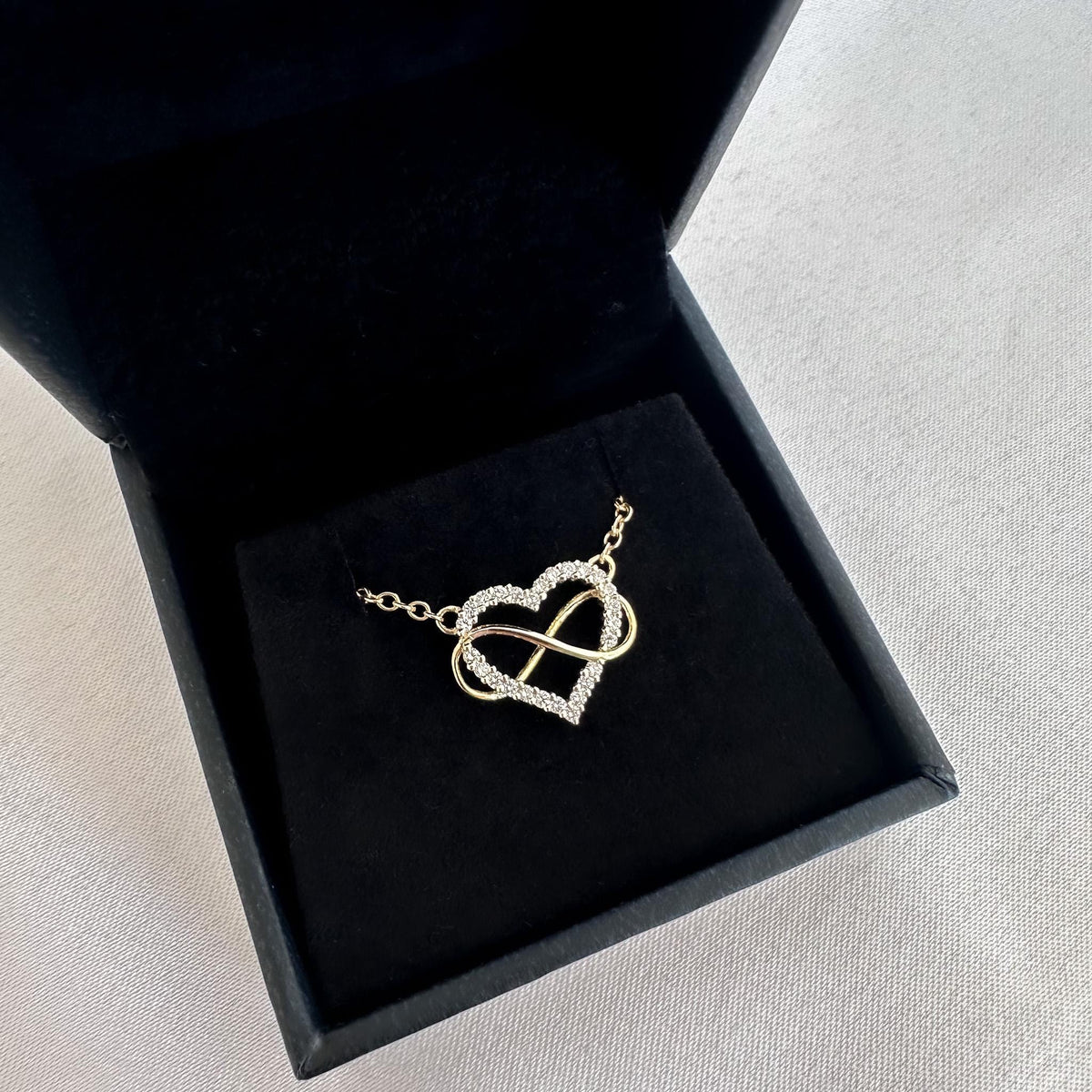 Diamond heart infinity necklace in a black jewelry box on a light gray surface