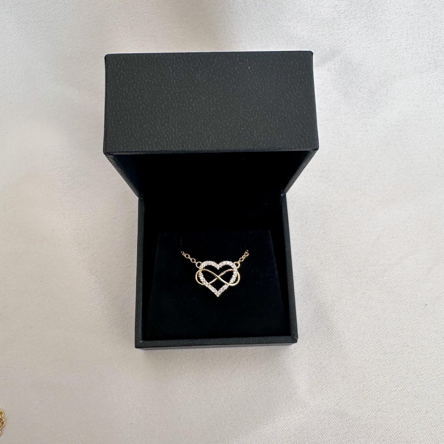 Gold heart-shaped necklace in a black jewelry box on a light gray background