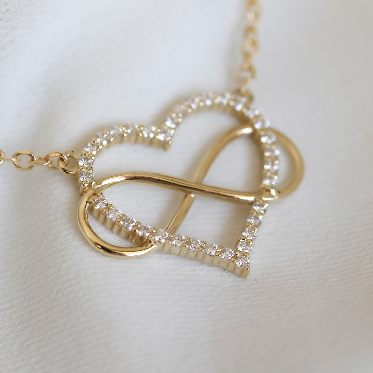 Close-up of an open heart set with round diamonds in shared prongs, wrapped in a gold infinity loop
