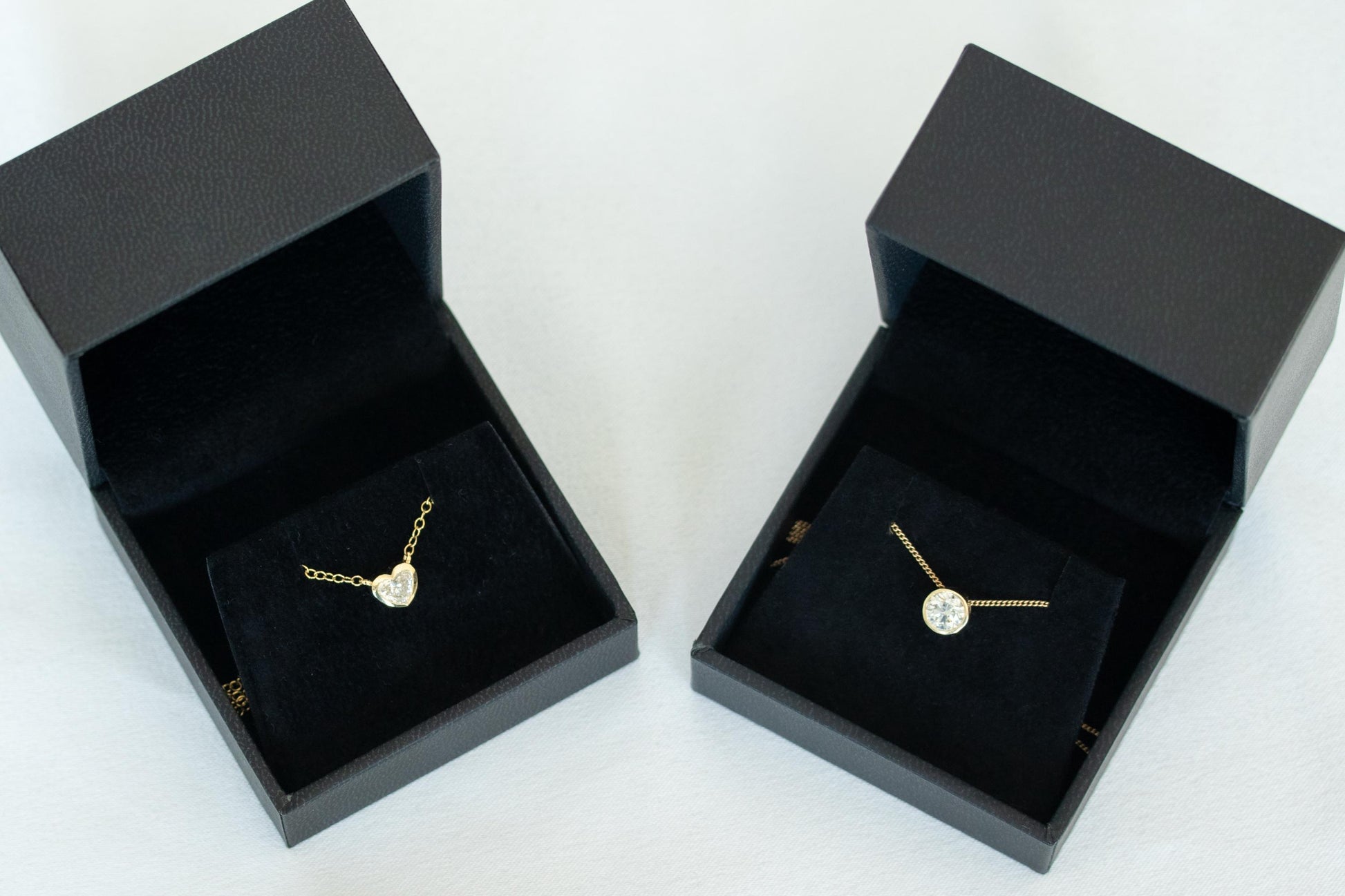 Two gold necklaces in black jewelry boxes on a white background