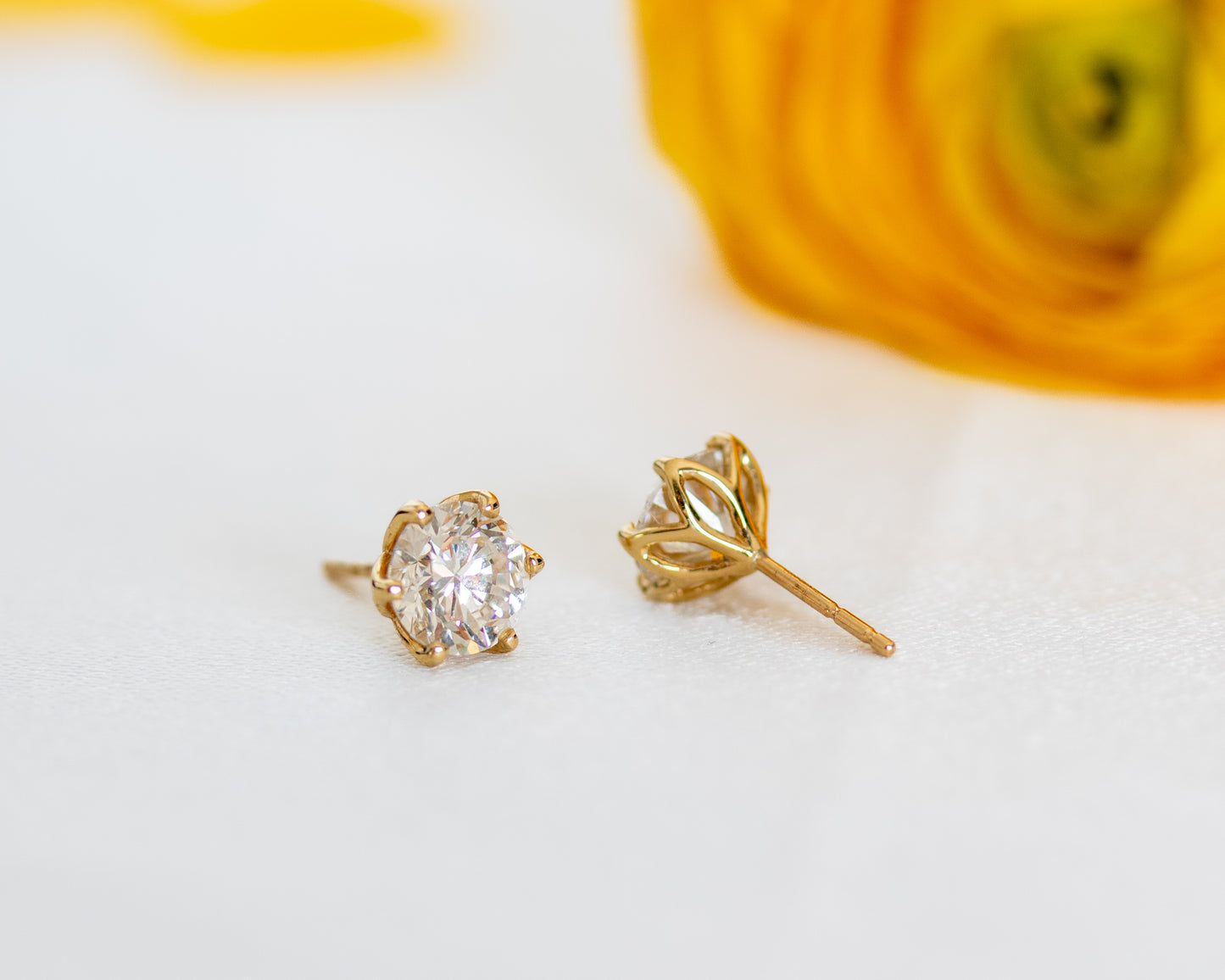 Round diamond stud earrings in 14K gold beside a yellow flower