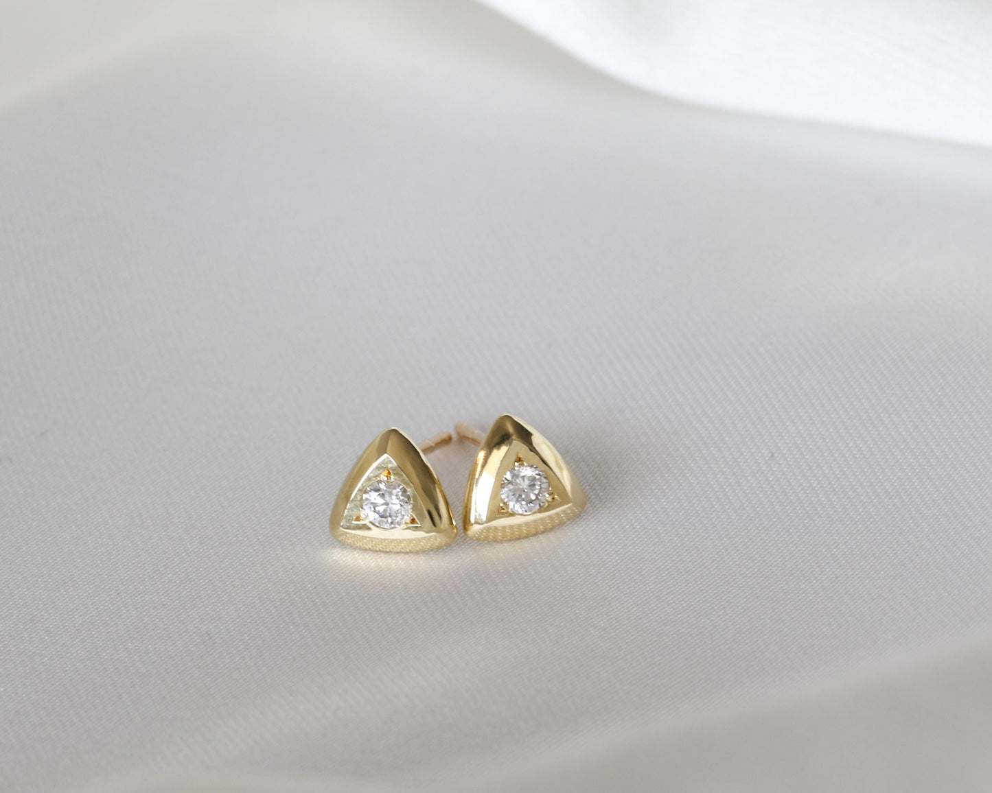 Diamond triangle stud earrings in gold, shown on white silk