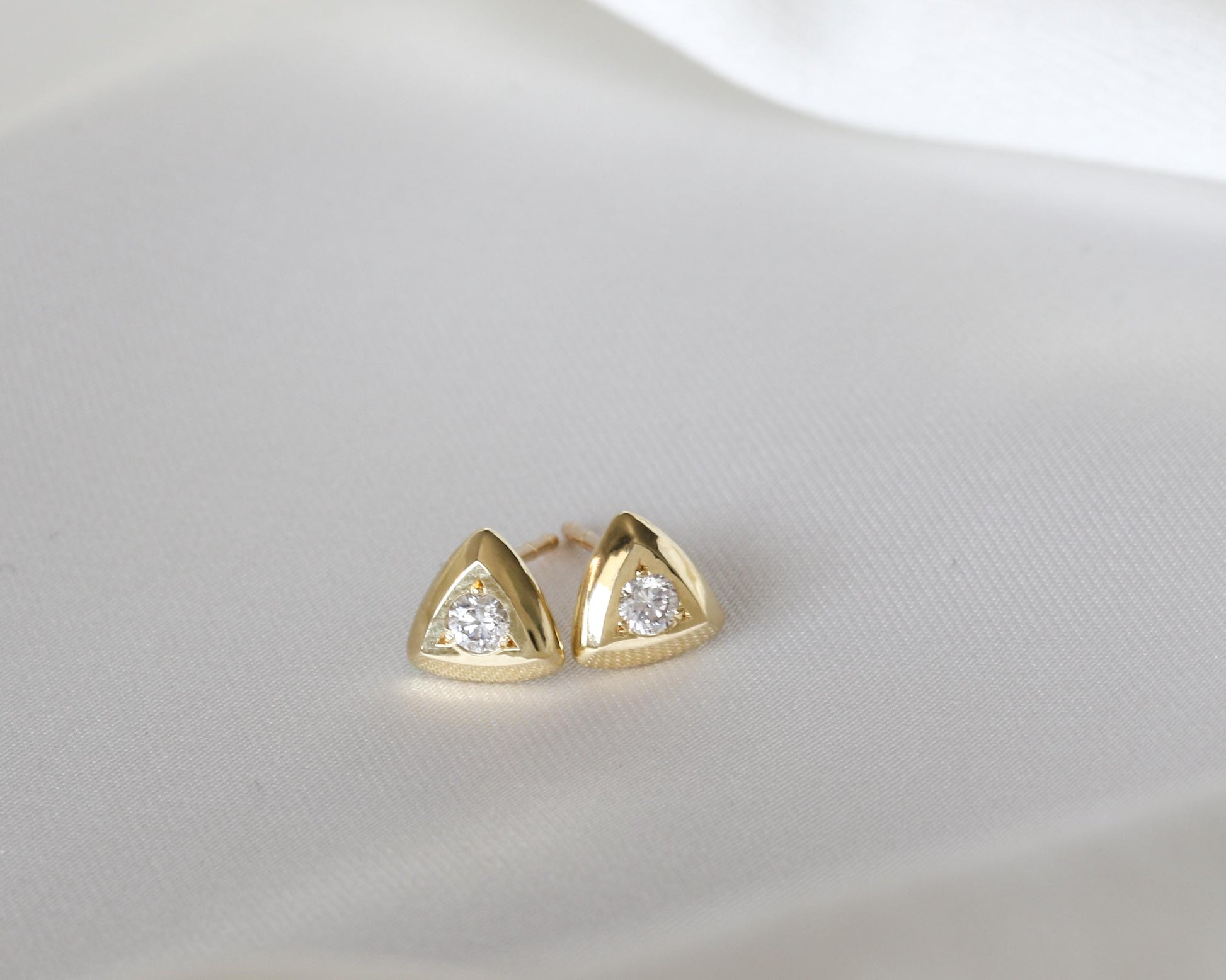 Diamond triangle stud earrings in gold, shown on white silk
