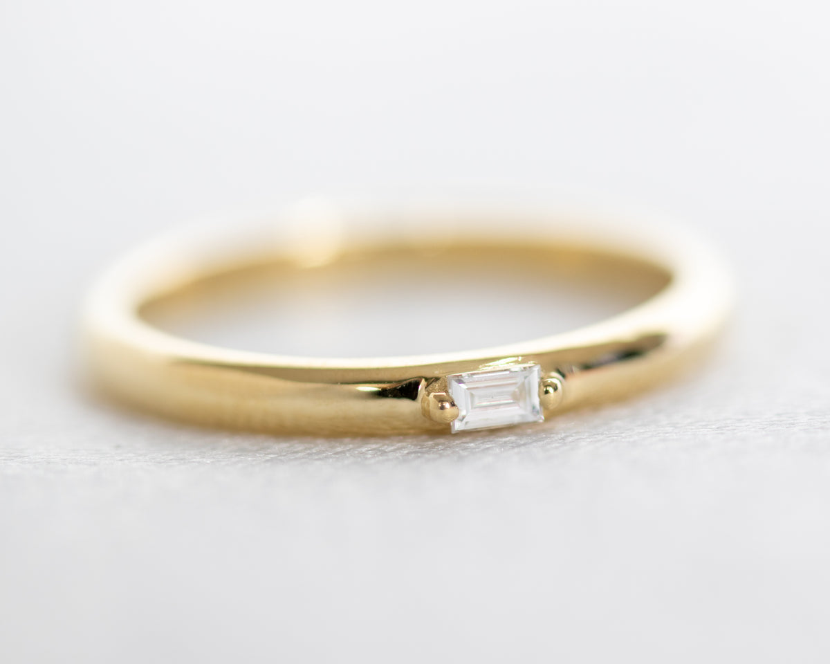 Domed yellow gold band with a prong-set baguette diamond, angled view on white