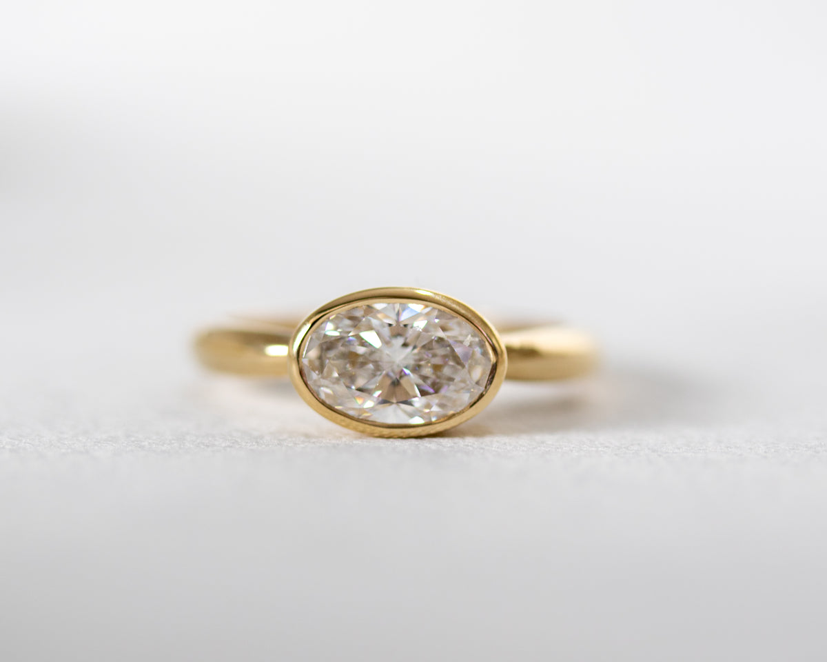 East-west oval diamond in a bezel setting, yellow gold engagement ring, front view.