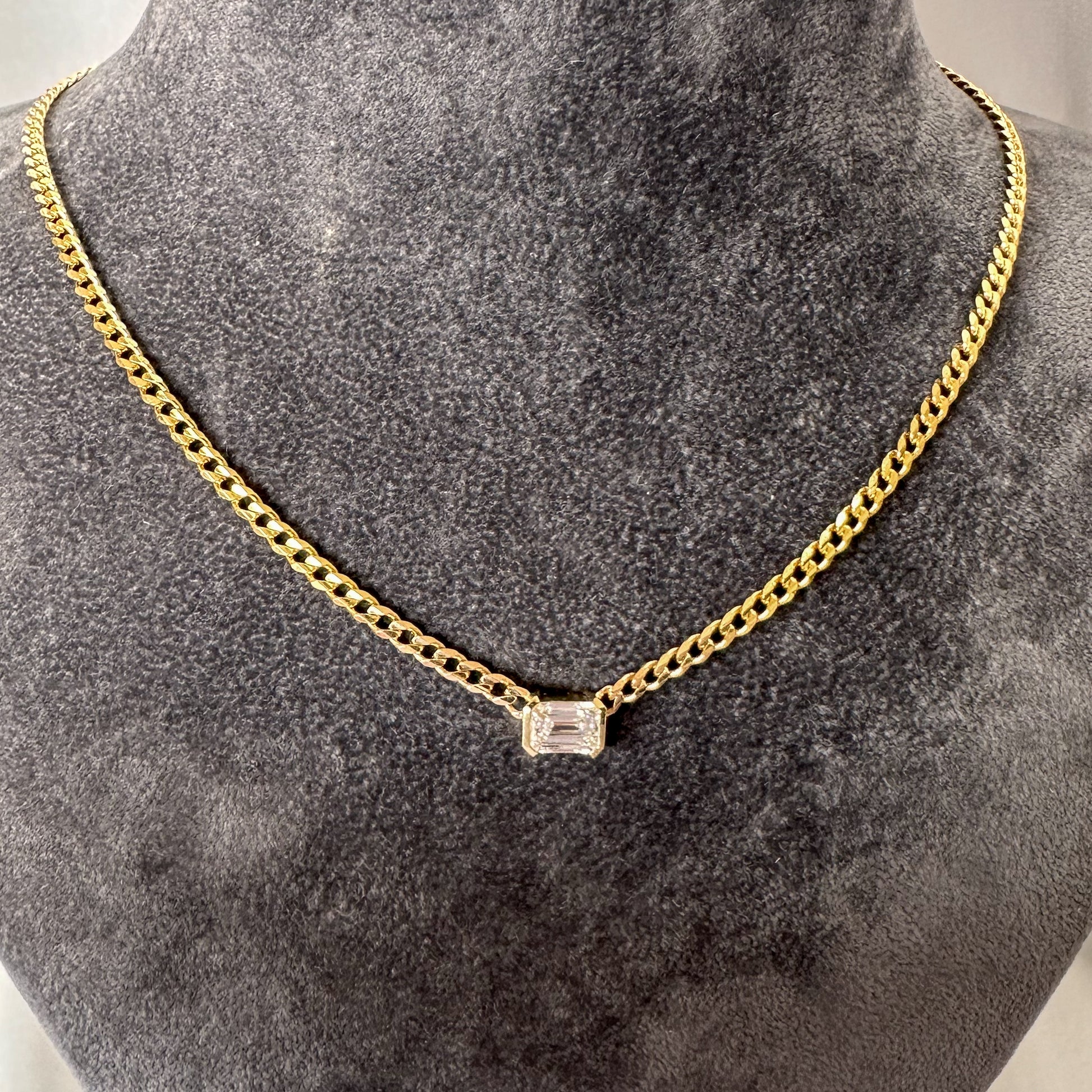 A 14K gold diamond solitaire necklace with an emerald cut natural diamond pendant on a gray textured jewelry torso