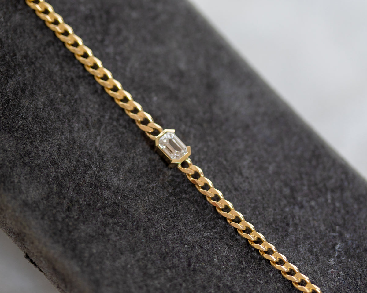 Emerald cut diamond curb chain bracelet on a gray surface