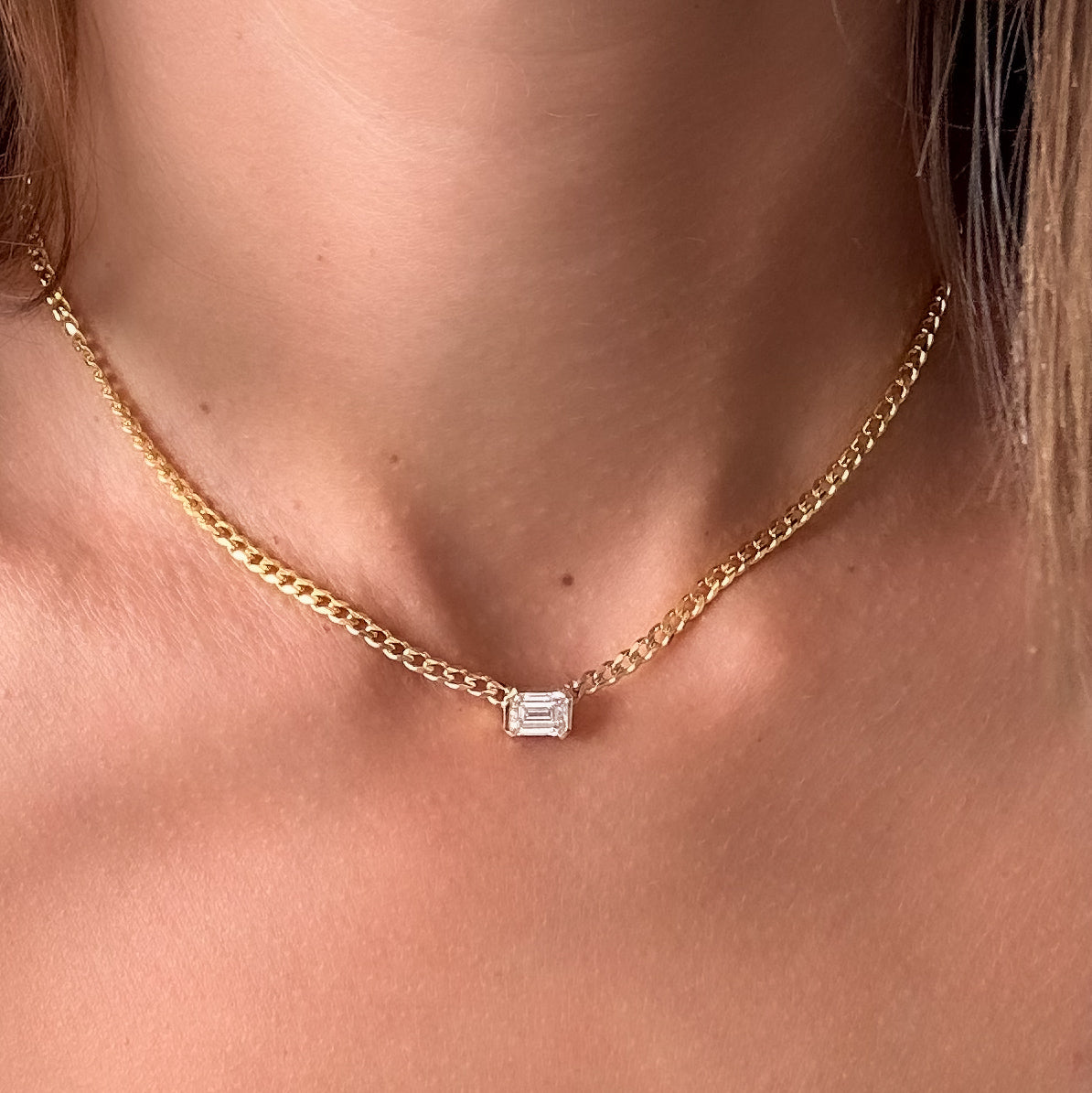 Emerald cut diamond choker on a fine 14K gold curb chain, worn on the neck, close-up