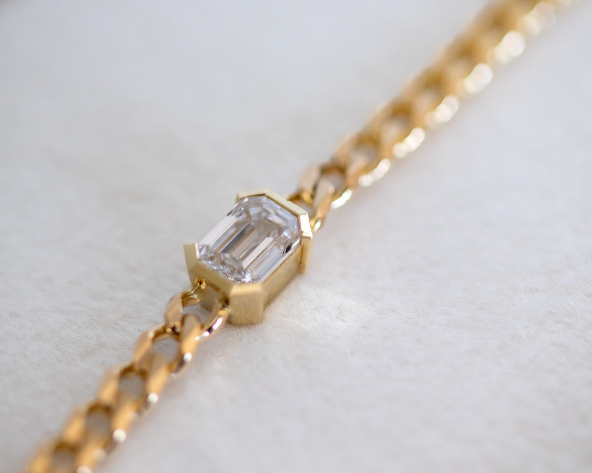 14K gold curb chain bracelet with an emerald cut diamond on a light background