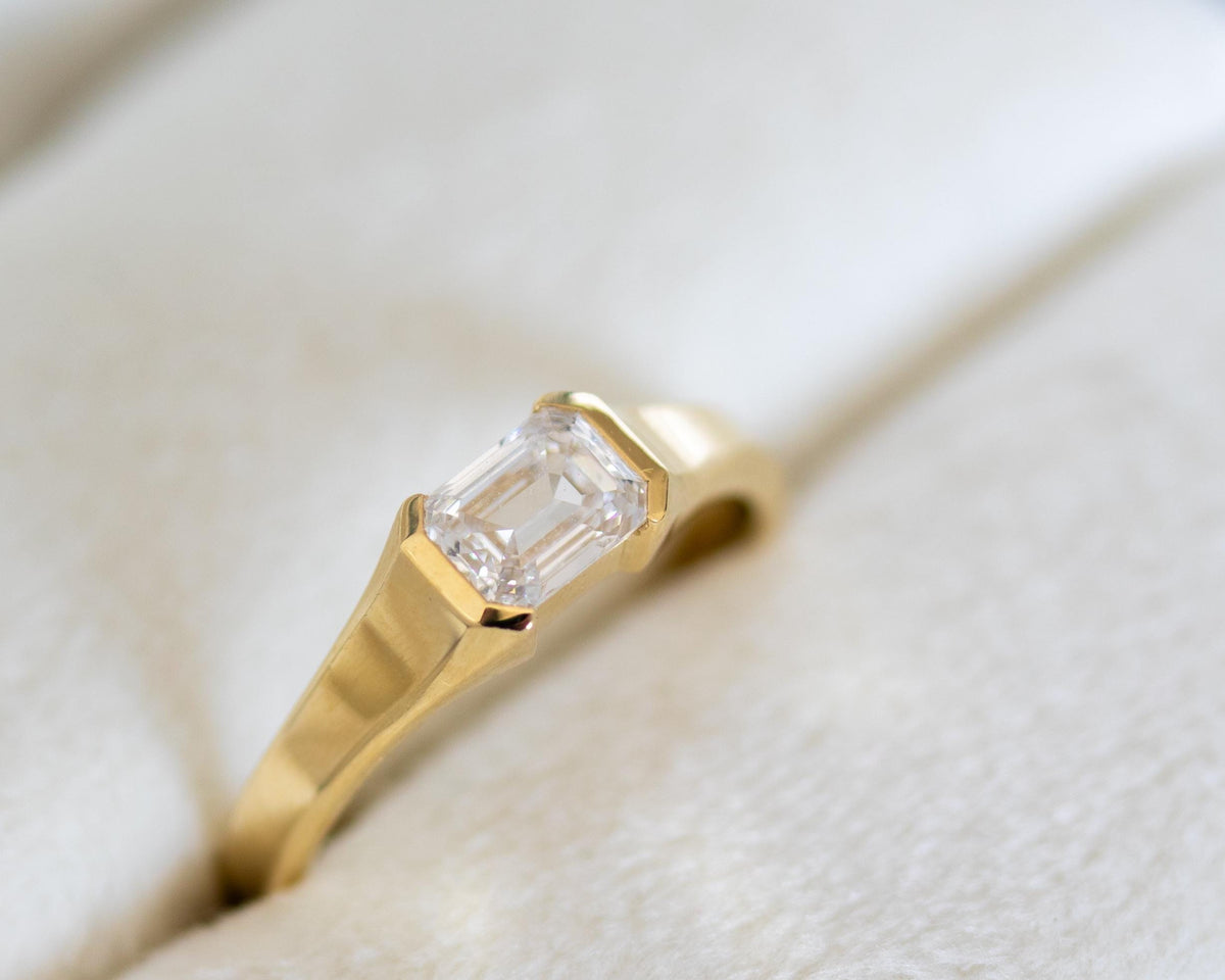 Emerald cut diamond solitaire ring in a 14K yellow gold half bezel