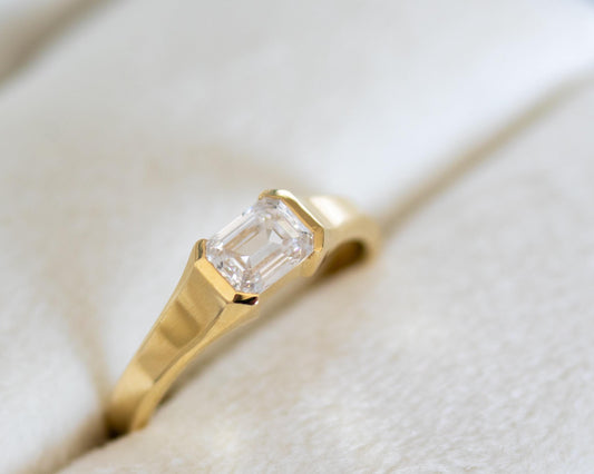 Emerald cut diamond solitaire ring in a 14K yellow gold half bezel