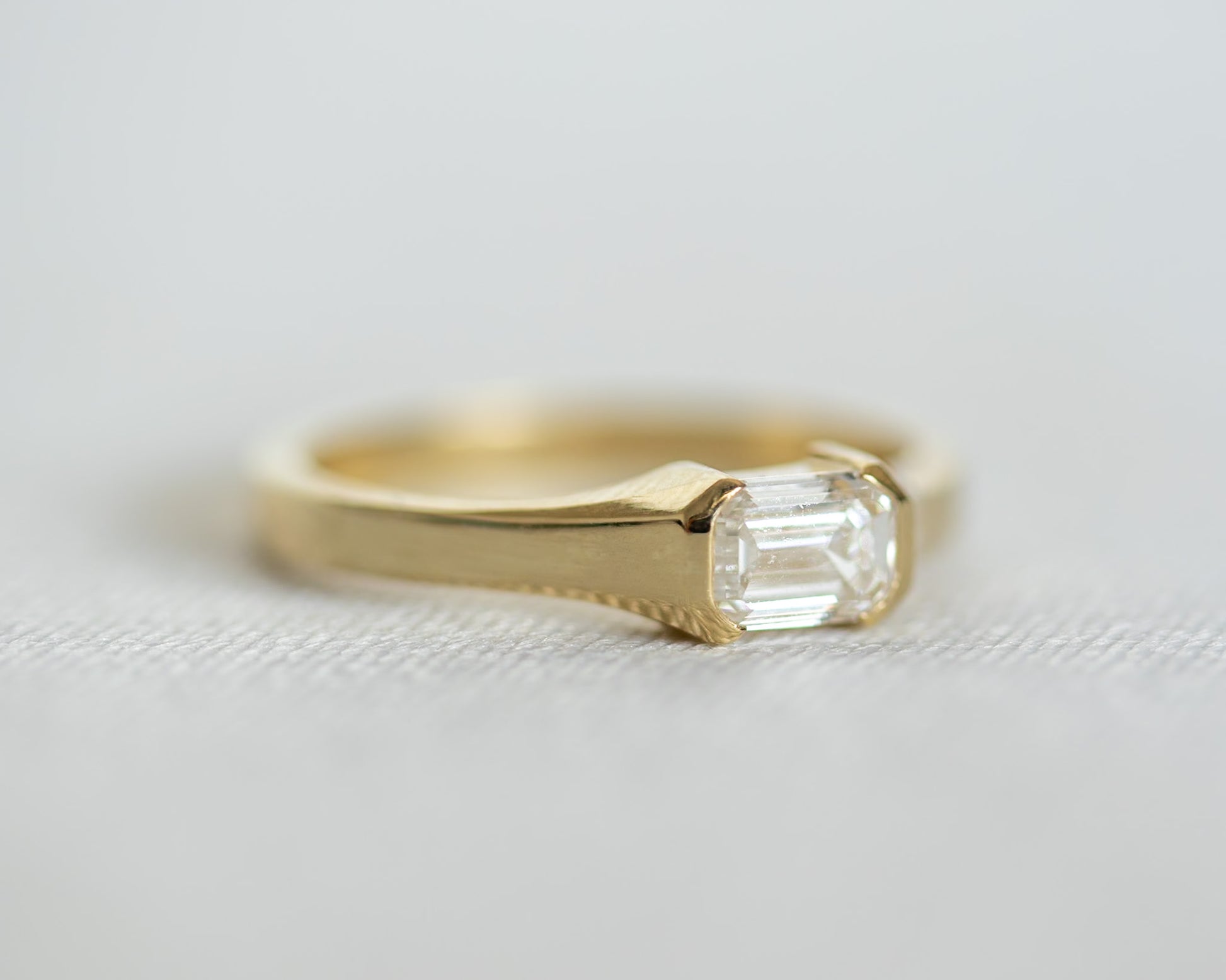 Gold ring with a emerald cut diamond on a light gray background