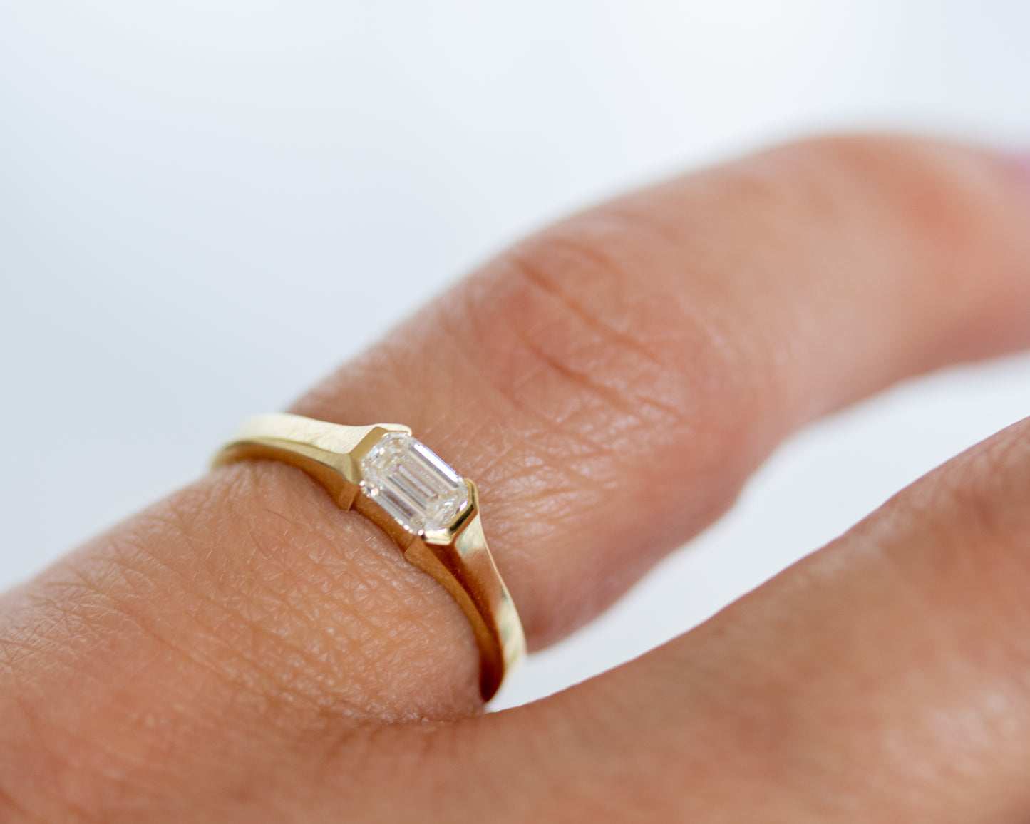 Gold ring with a diamond on a finger against a white background