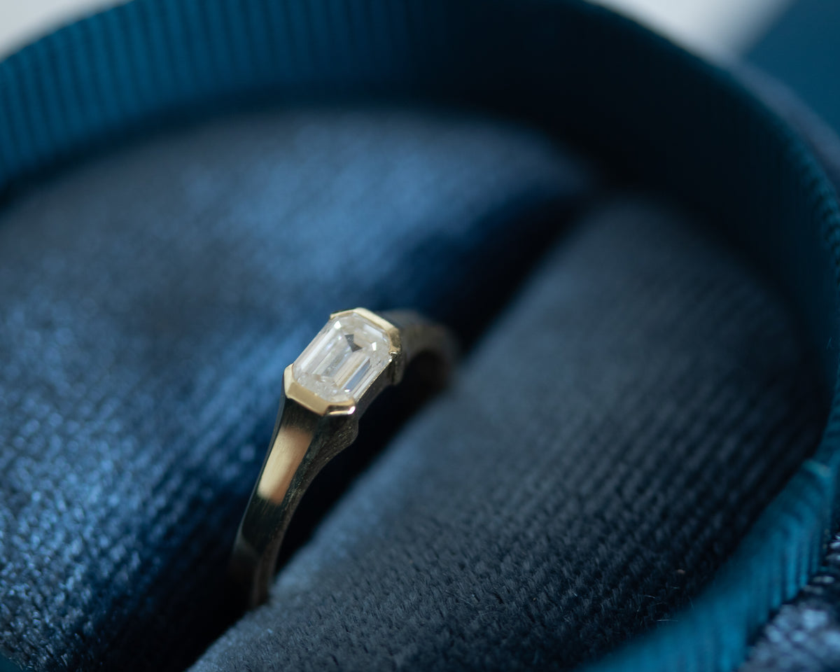 Emerald cut diamond pinky ring in 14K yellow gold on a blue textured surface