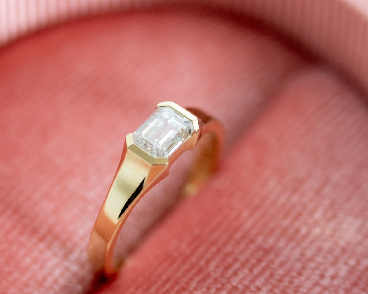 0.50 ct emerald cut diamond ring in 14K yellow gold on pink fabric, close-up