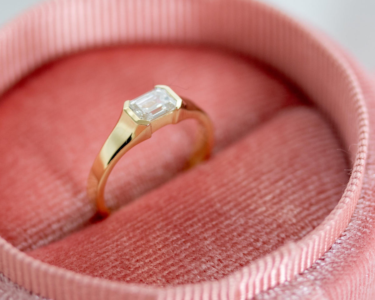 Emerald cut diamond half bezel ring in 14K yellow gold on pink fabric