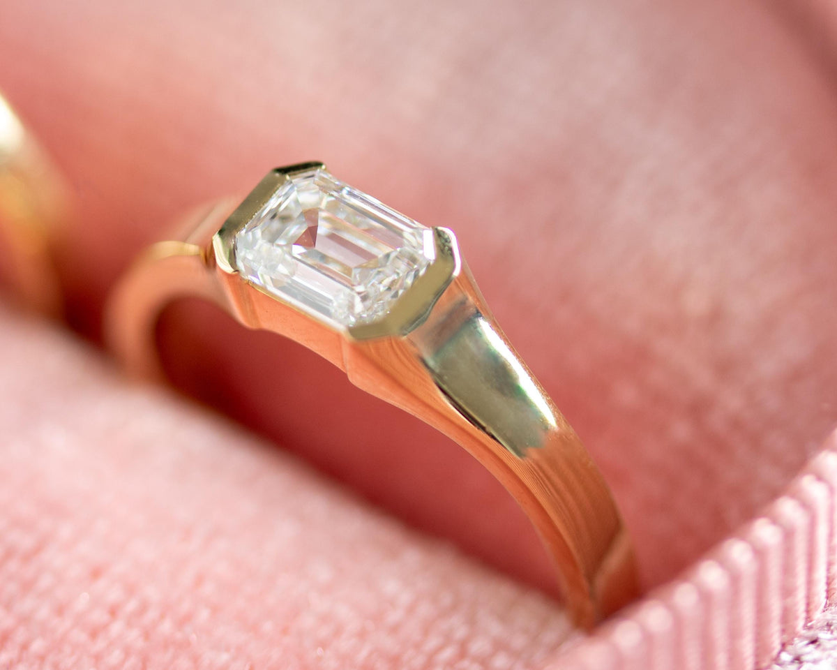 Emerald cut diamond half bezel solitaire ring, worn on the finger
