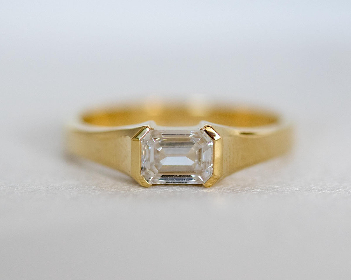 Emerald cut diamond in a 14K yellow gold half bezel, step-cut facets close-up