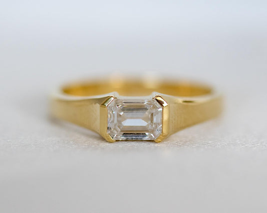 Emerald cut diamond in a 14K yellow gold half bezel, step-cut facets close-up