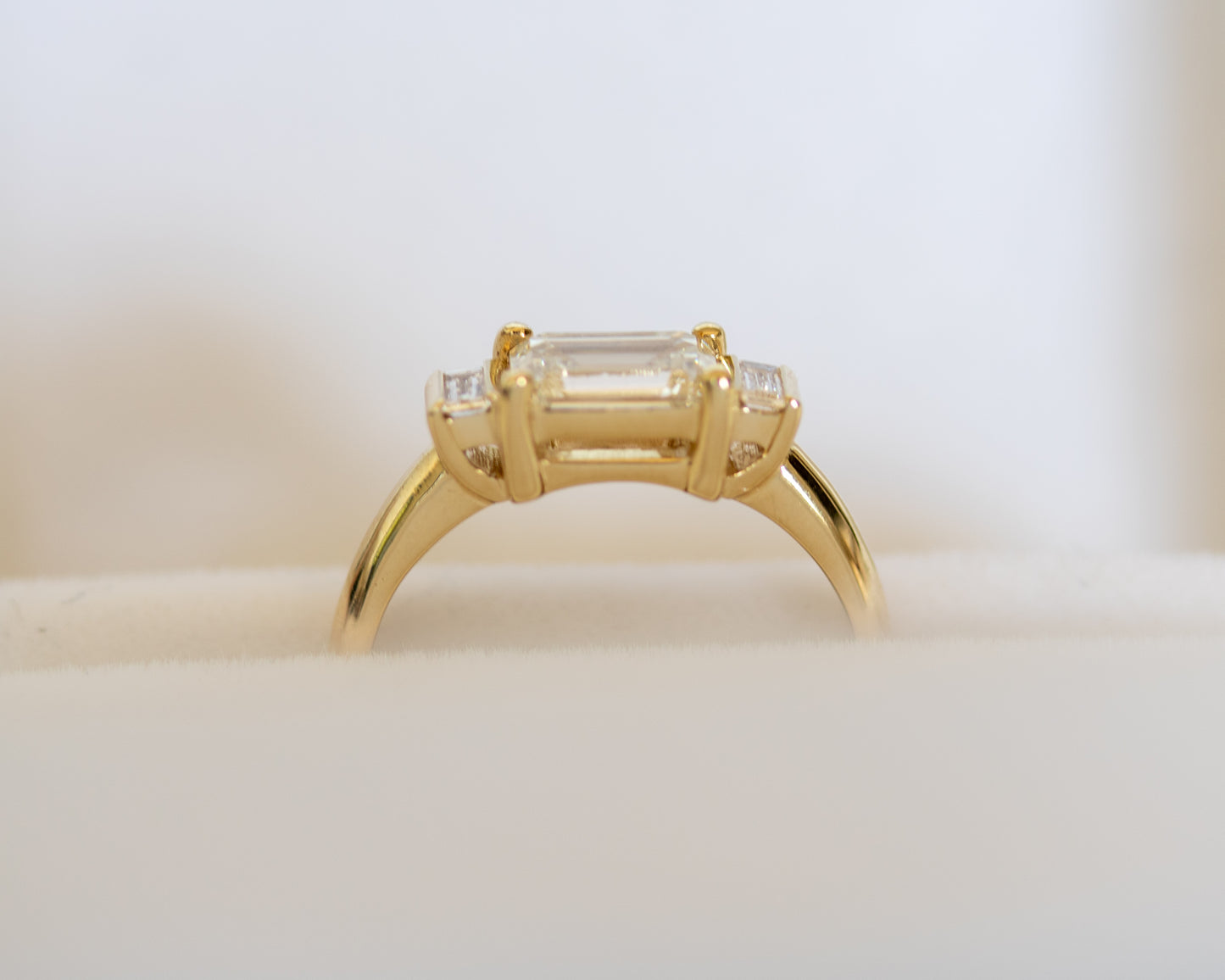 Emerald cut diamond trilogy ring in 14K yellow gold, side view
