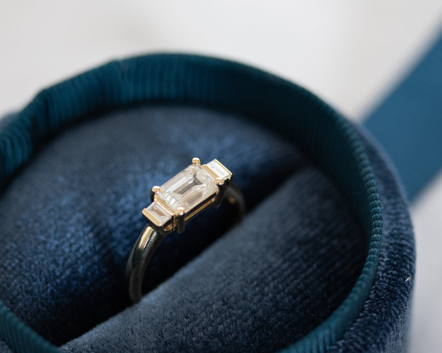 Emerald cut diamond trilogy ring in dark blue velvet box