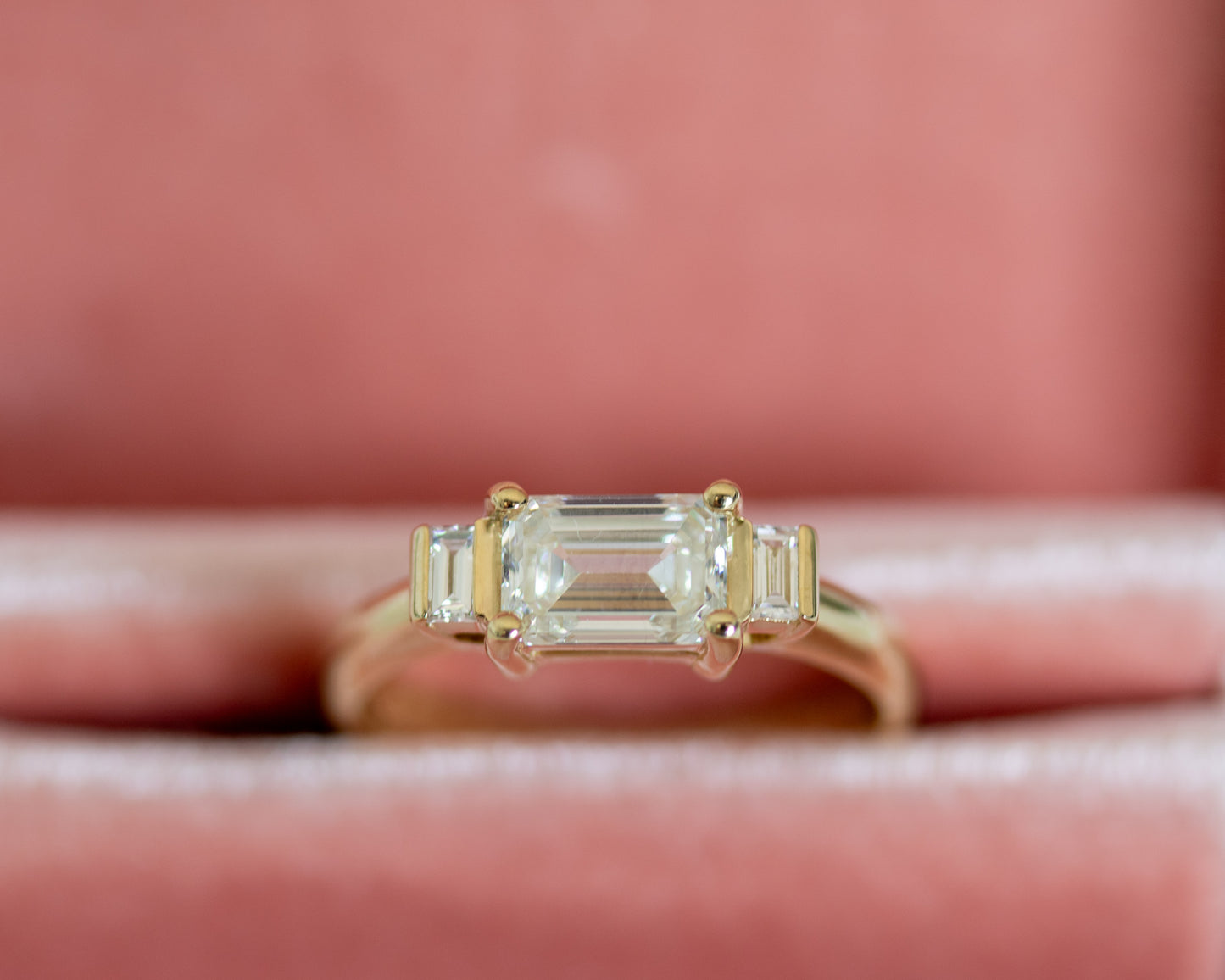 Emerald cut diamond trilogy ring on pink surface
