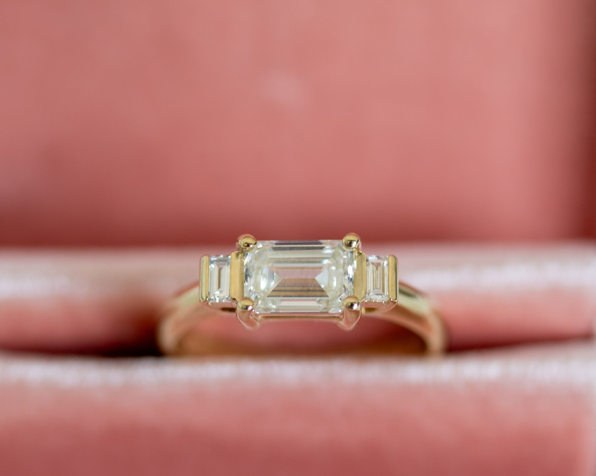 Emerald cut diamond trilogy ring on pink surface