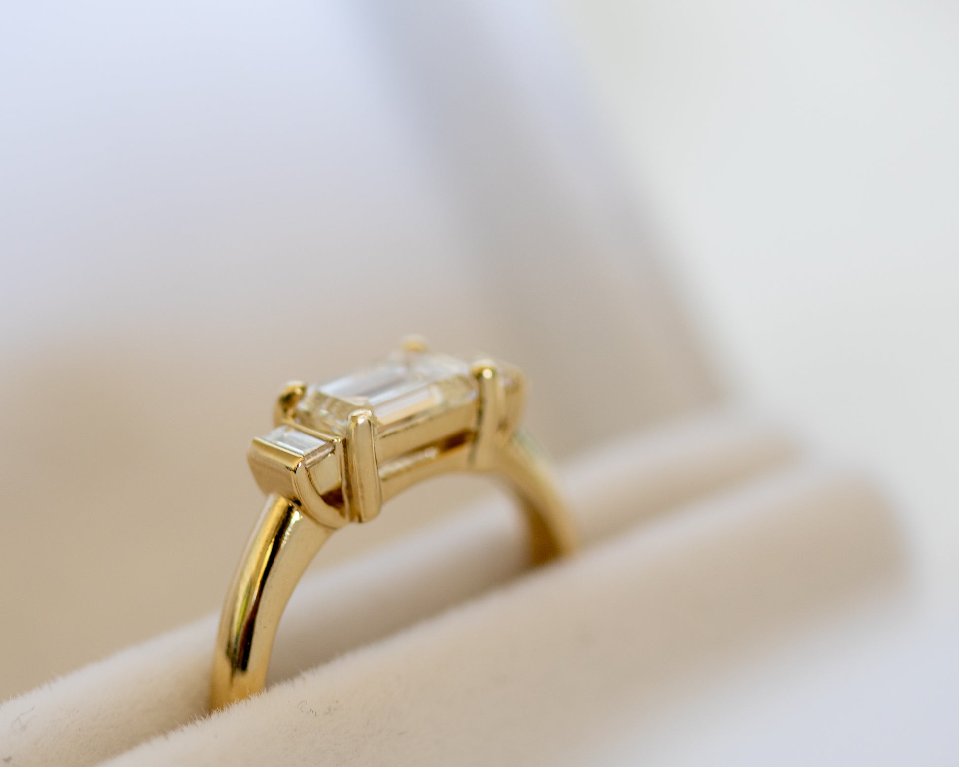 Emerald cut diamond trilogy ring in 14K yellow gold on white surface