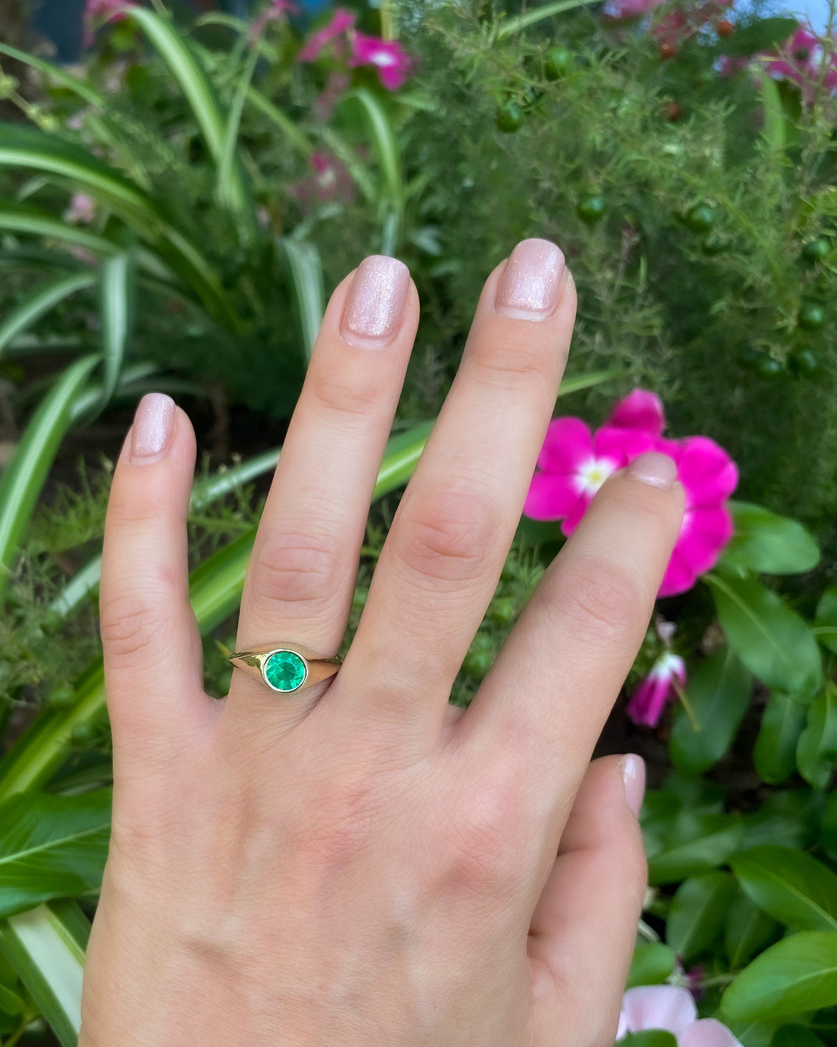 Yellow gold emerald signet ring worn on the hand, outdoors among flowers