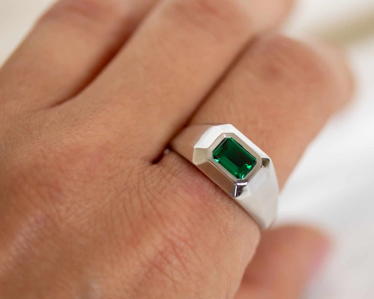 White gold emerald signet ring worn on a man’s hand, modern geometric style