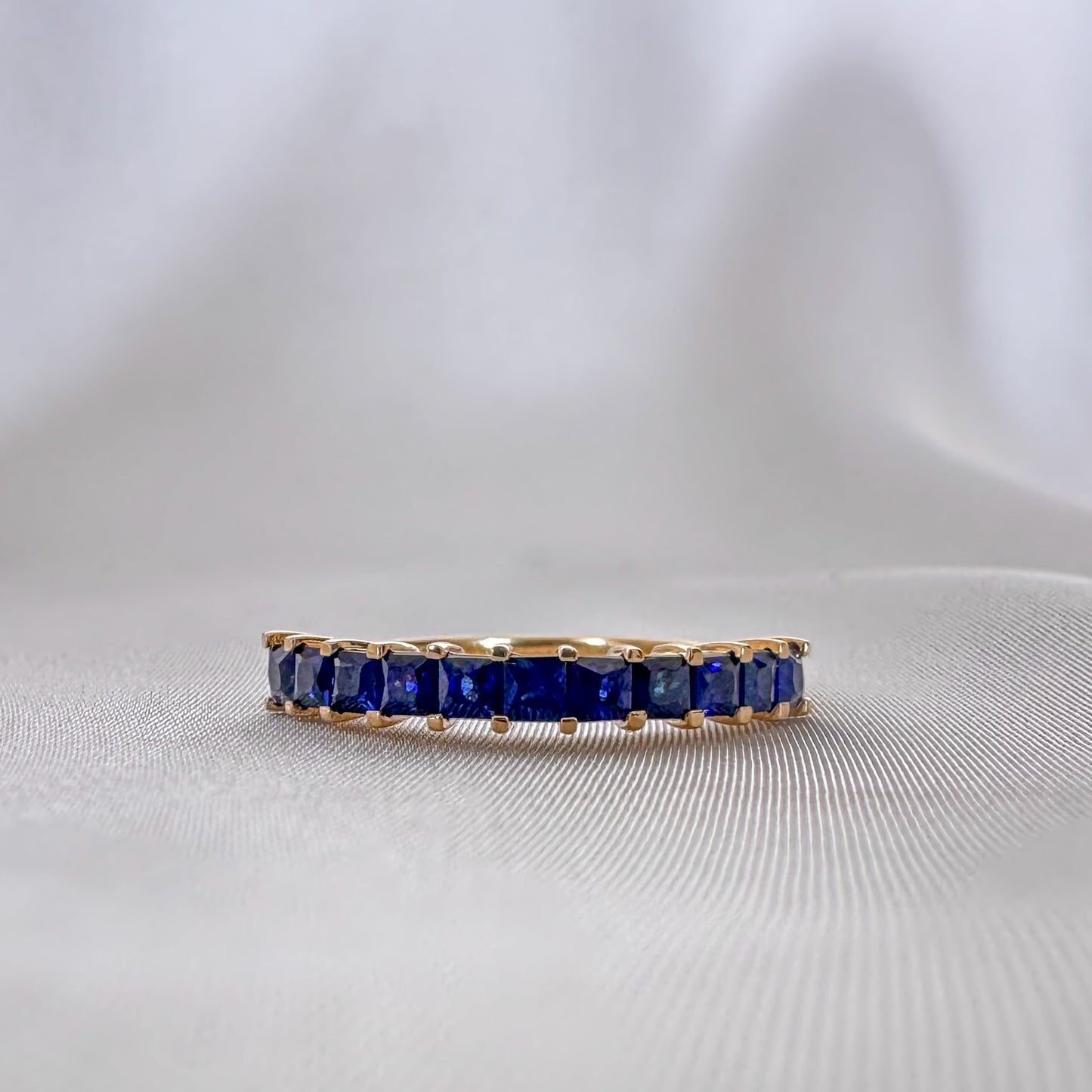 blue sapphires princess cut eternity ring set in 14k gold on white background