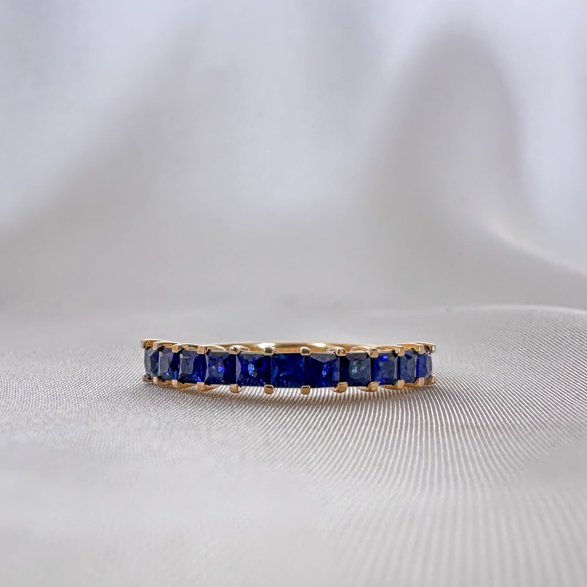 blue sapphires princess cut eternity ring set in 14k gold on white background