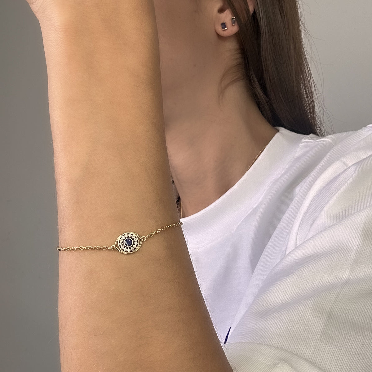 14K yellow gold evil eye bracelet with a blue sapphire and diamond halo on the wrist, arm view