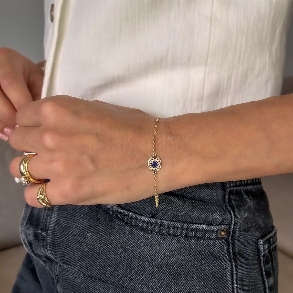 14K yellow gold evil eye bracelet with a blue sapphire and diamond halo, worn on the wrist