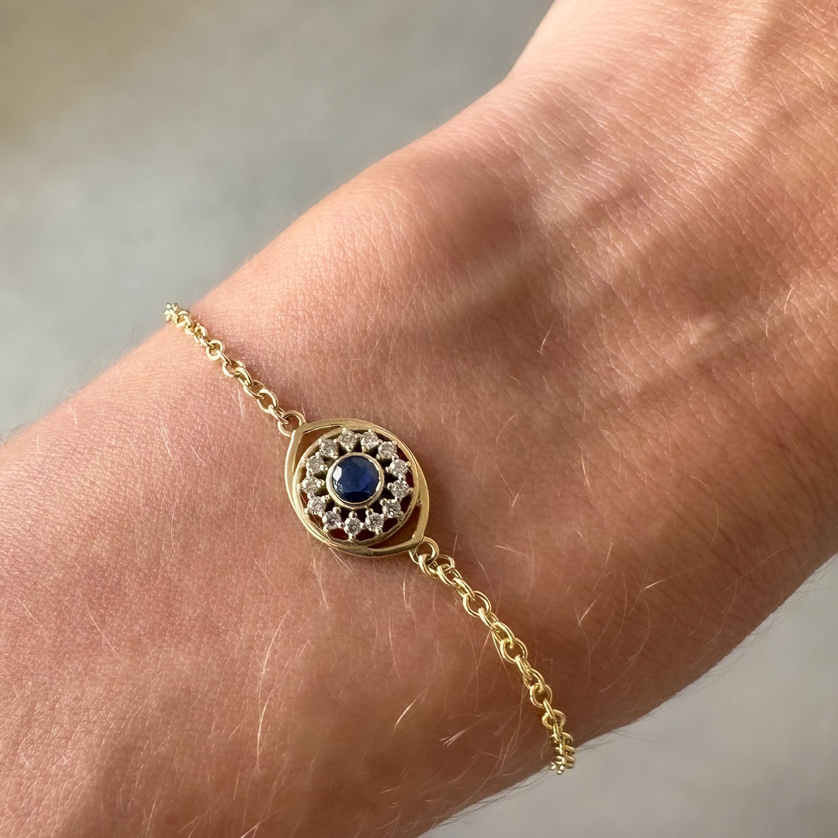 Close-up of a 14K yellow gold evil eye with a blue sapphire and diamond halo on the wrist