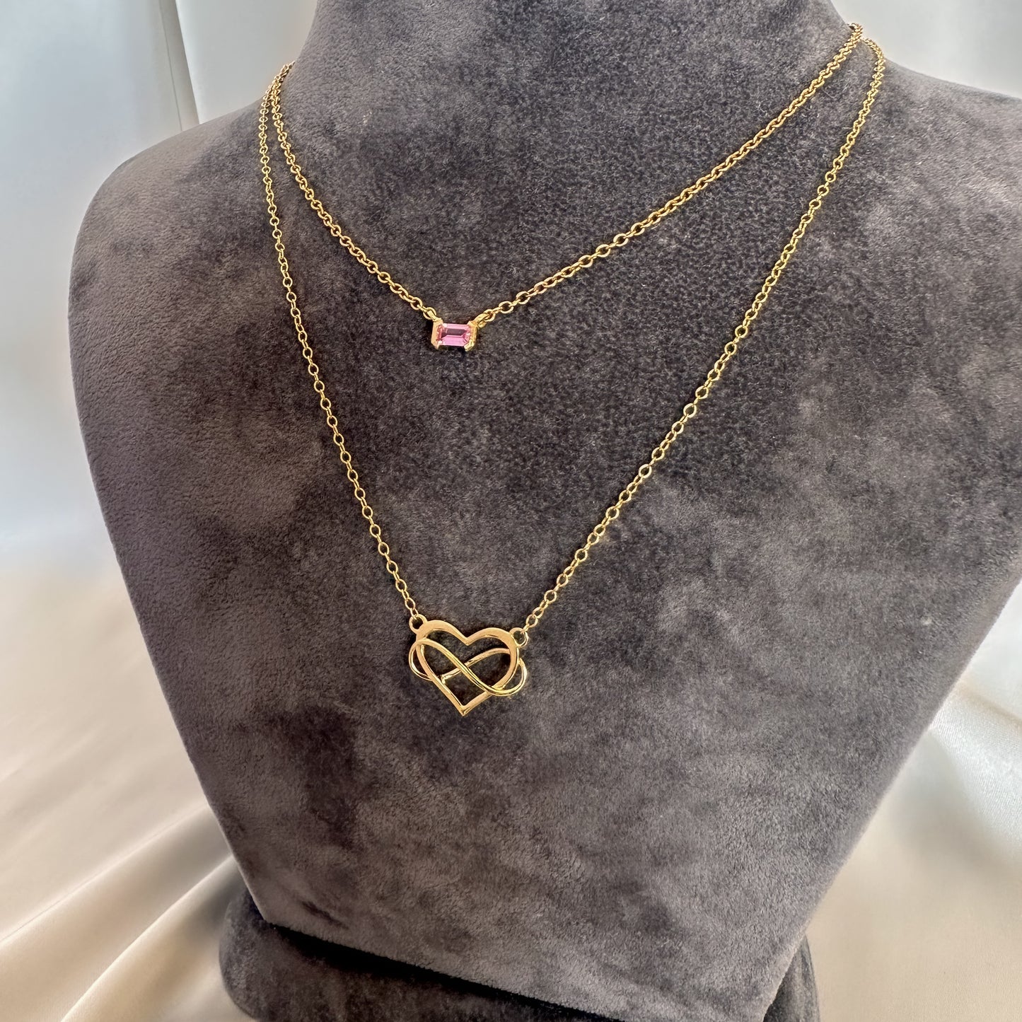 yellow gold heart and infinity symbol pendant and chain and yellow gold pink sapphire choker on gray velvet tourso