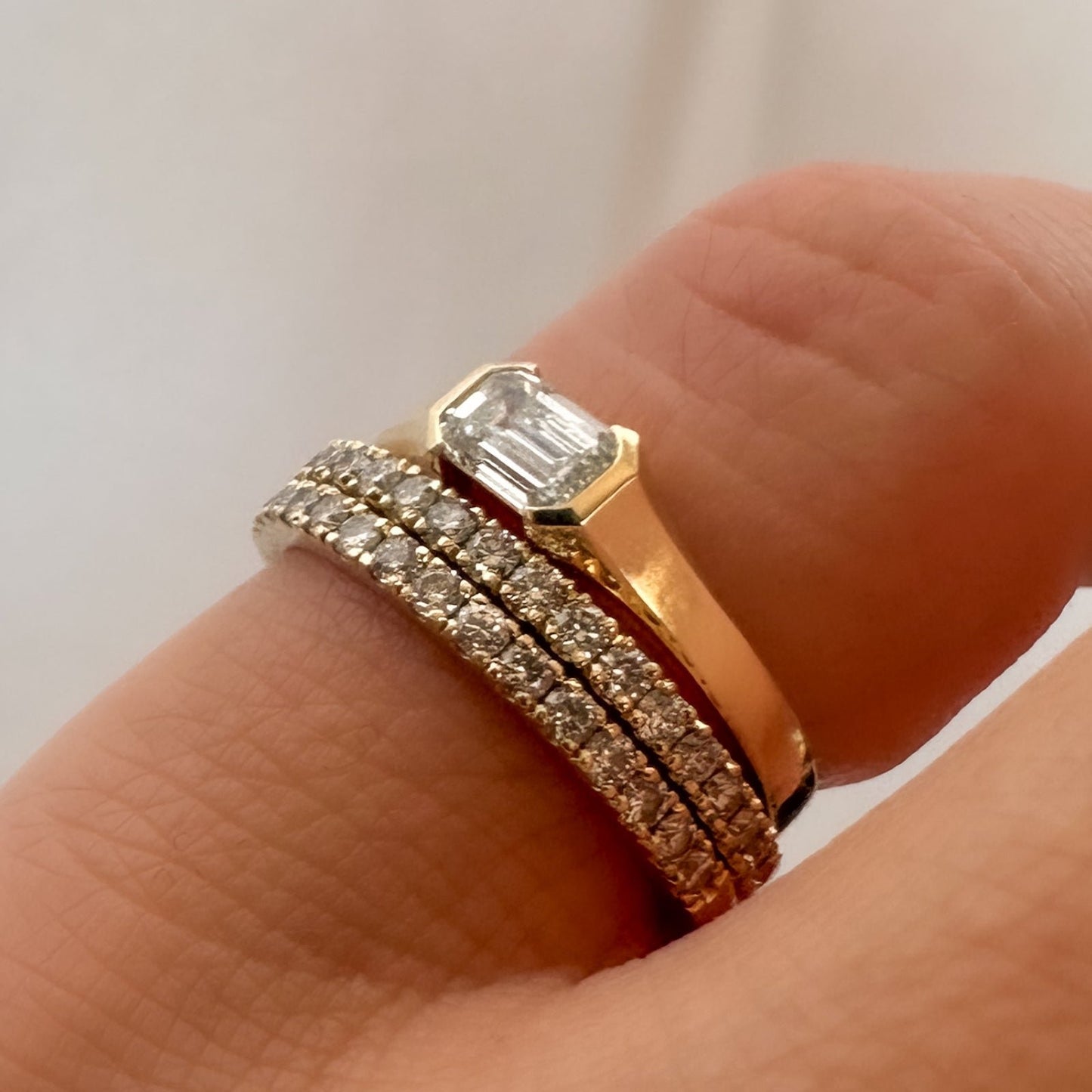 three gold rings, two diamond eternity rings and one solitaire emerald cut diamond ring stacked on pinky finger
