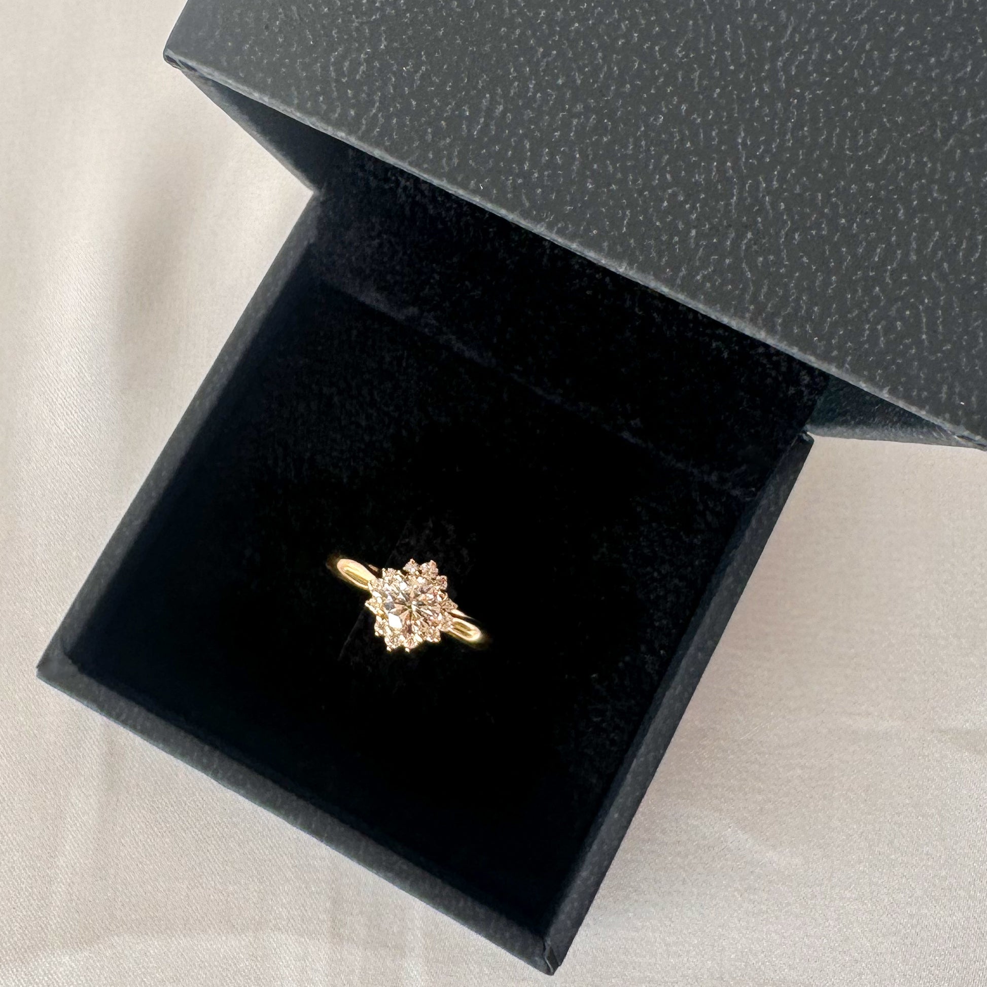 A floral engagement ring with a central diamond and smaller surrounding diamonds set in a 14K gold band in a black velvet box.