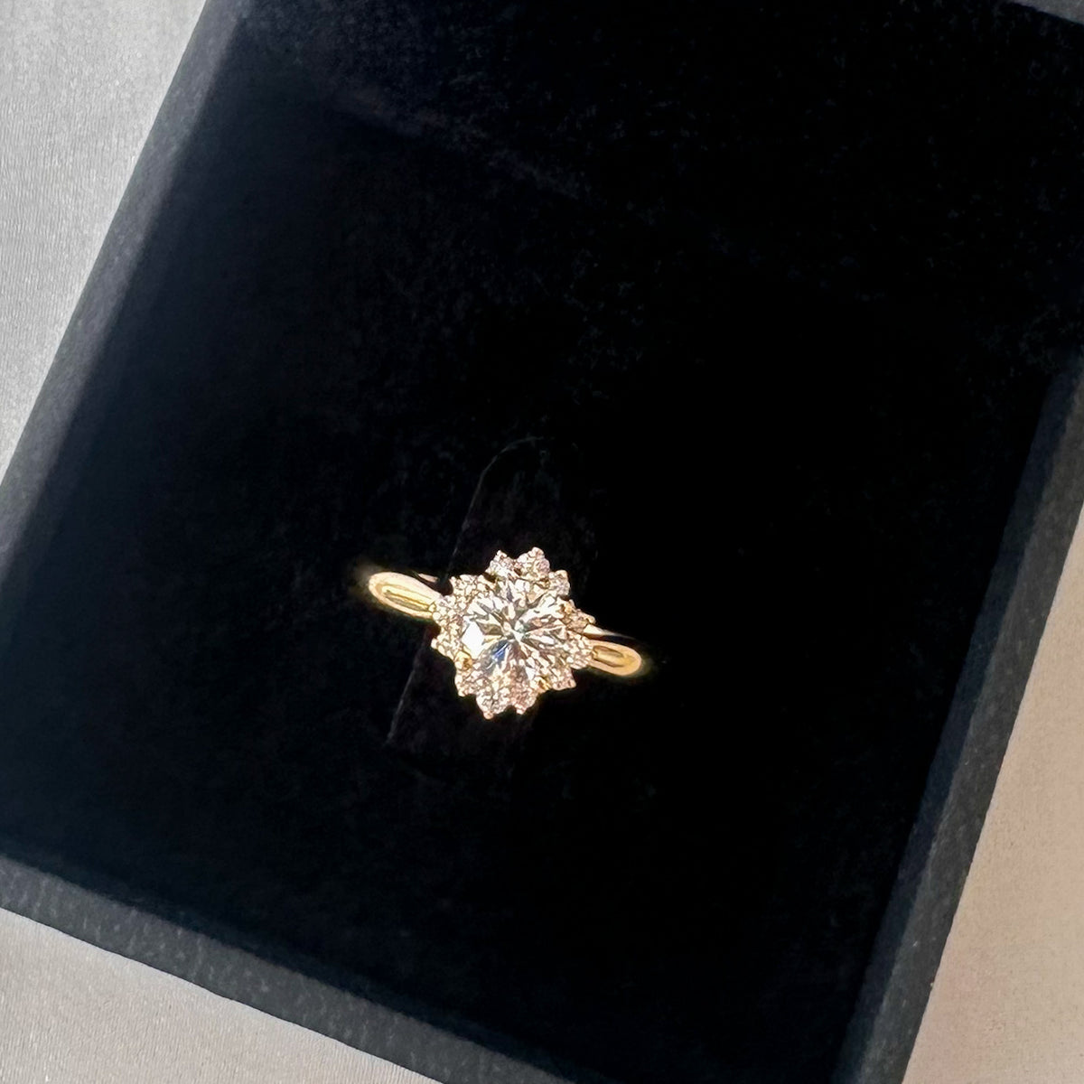 Close-up of a floral diamond halo ring in yellow gold in a black jewelry box
