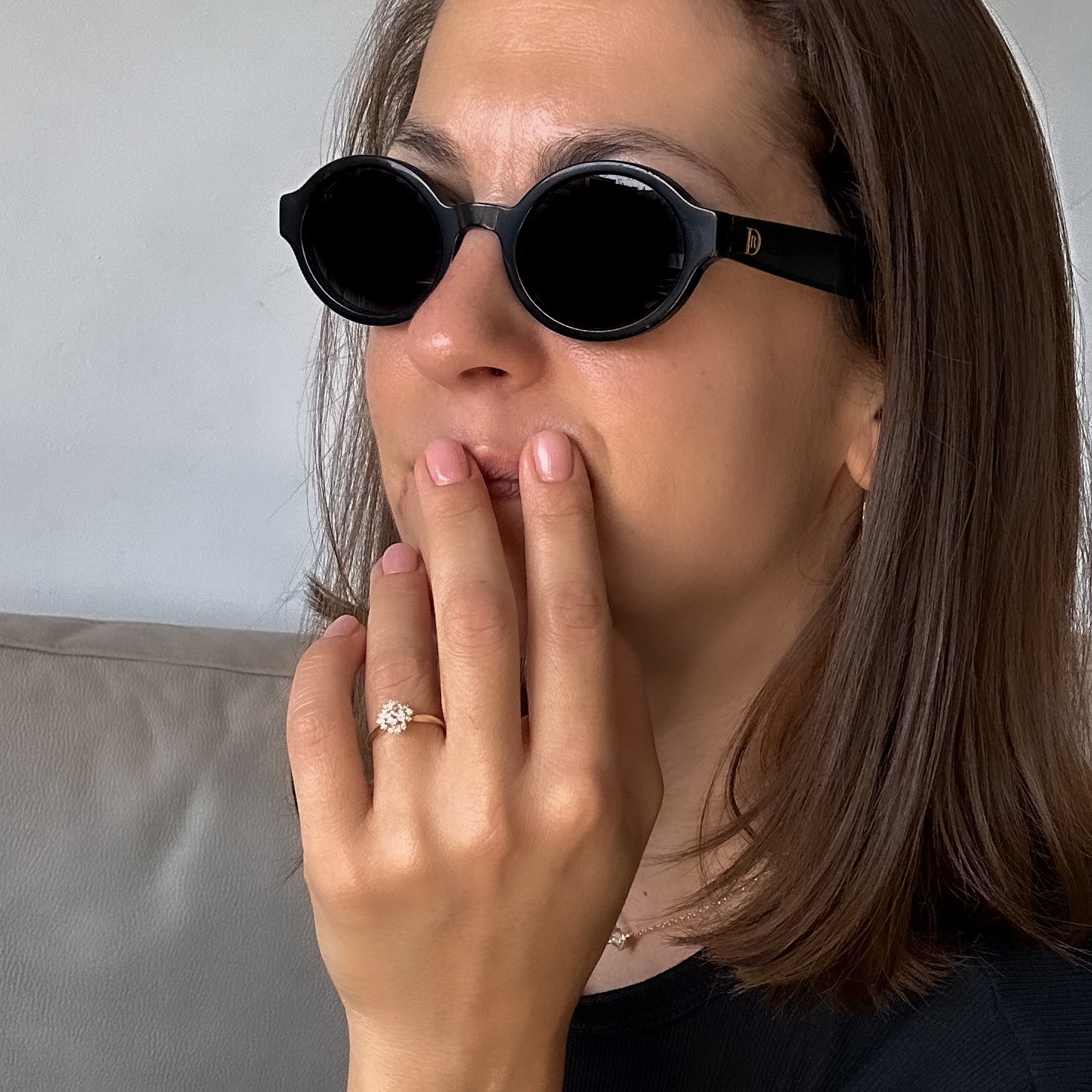 A women with sunglasses putting hand gently on her face wearing a floral engagement ring with a central diamond and smaller surrounding diamonds set in a 14K gold band in a black velvet box.