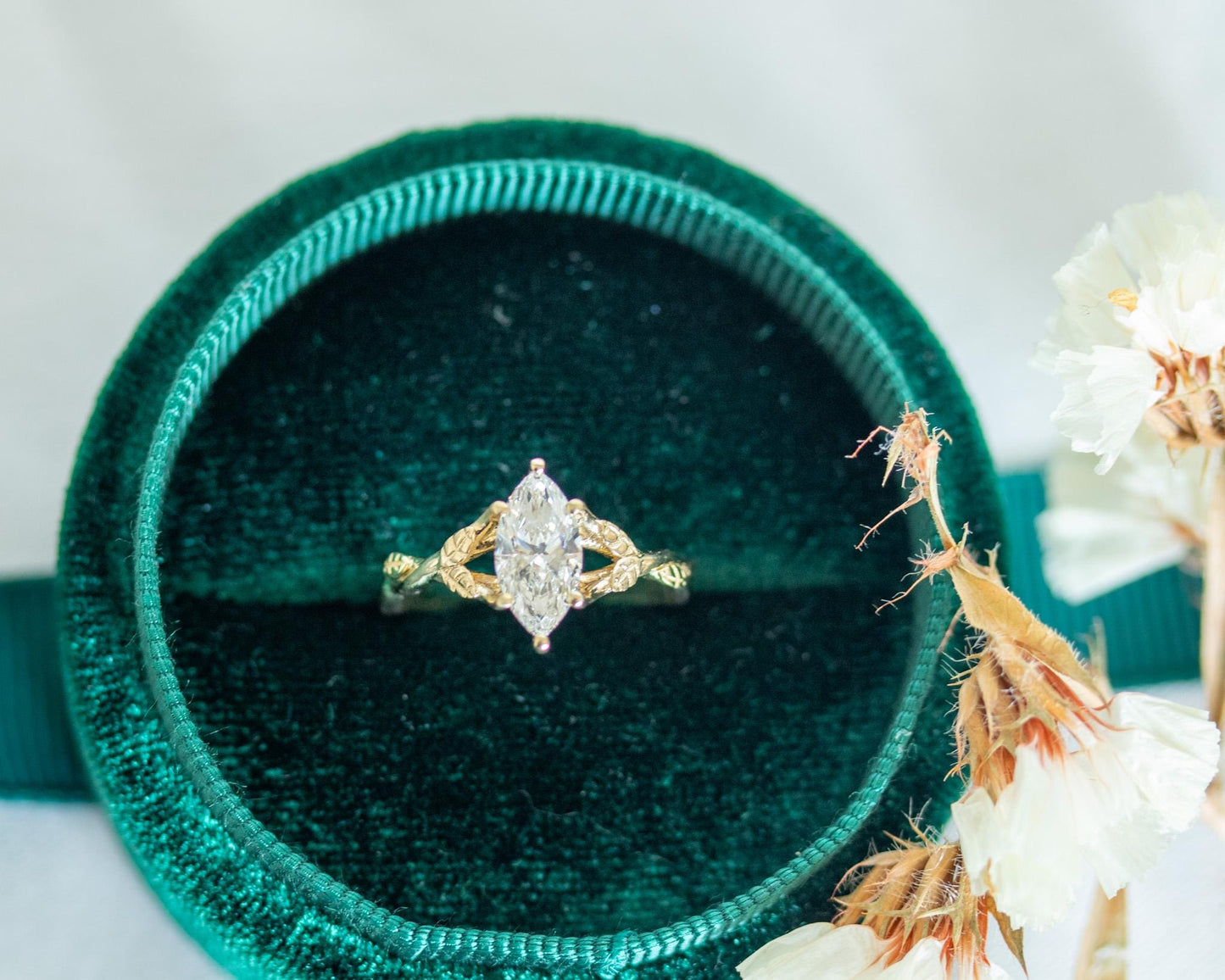 Gold ring with a diamond on a green velvet cushion next to white flowers.