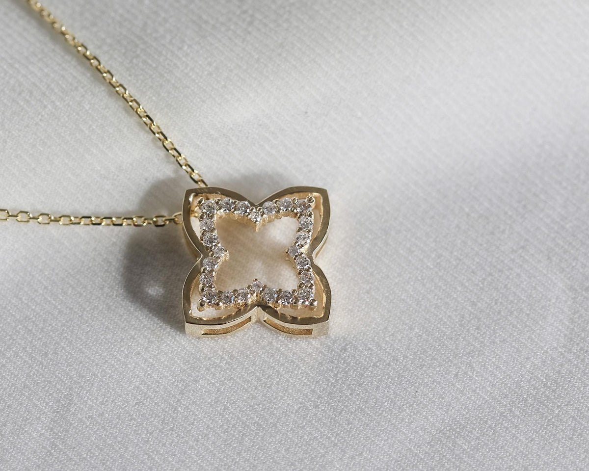 Angled view of a 14K yellow gold open four-leaf clover pendant with diamonds on a light background