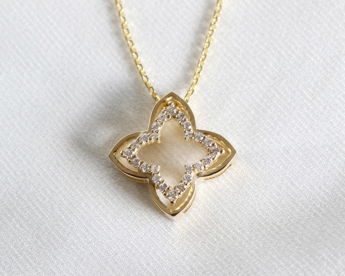 Close-up of a 14K yellow gold open four-leaf clover pendant with prong-set diamonds on white fabric